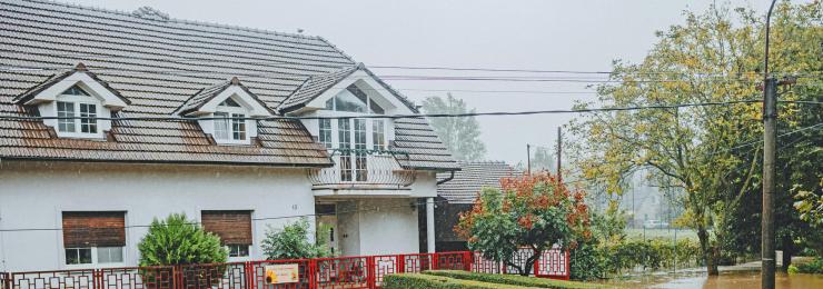 Überschwemmtes Wohnhaus mit überflutetem Vorgarten und braunem Hochwasser; Starkregen-Schaden, Symbolfoto.